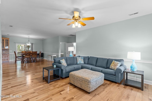 living room with light wood finished floors, baseboards, visible vents, and ceiling fan