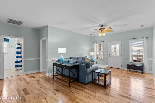 living room featuring light wood-type flooring, baseboards, visible vents, and a ceiling fan