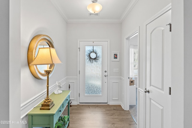 entrance foyer featuring a wainscoted wall, wood finished floors, visible vents, and ornamental molding