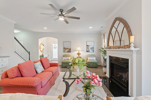 living room featuring arched walkways, stairway, crown molding, and wood finished floors