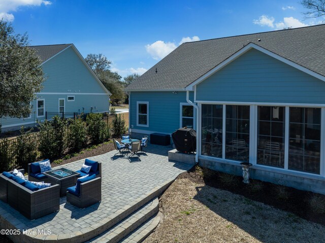 back of house featuring a patio, fence, an outdoor living space with a fire pit, roof with shingles, and a sunroom