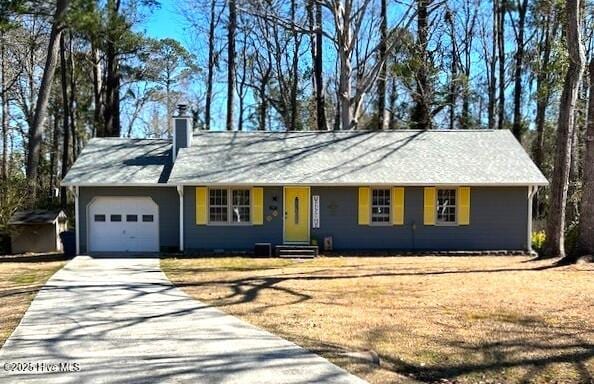 single story home with entry steps, an attached garage, concrete driveway, a chimney, and a front yard