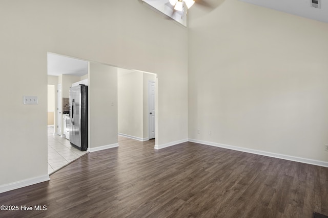 unfurnished living room featuring a ceiling fan, dark wood finished floors, a towering ceiling, and baseboards