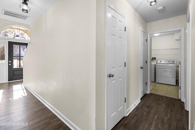 hallway with dark wood-type flooring, washing machine and clothes dryer, visible vents, and baseboards