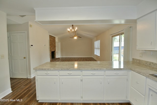 kitchen featuring a peninsula, dark wood-type flooring, white cabinetry, vaulted ceiling, and a brick fireplace