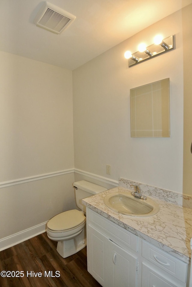 half bath featuring baseboards, visible vents, toilet, wood finished floors, and vanity