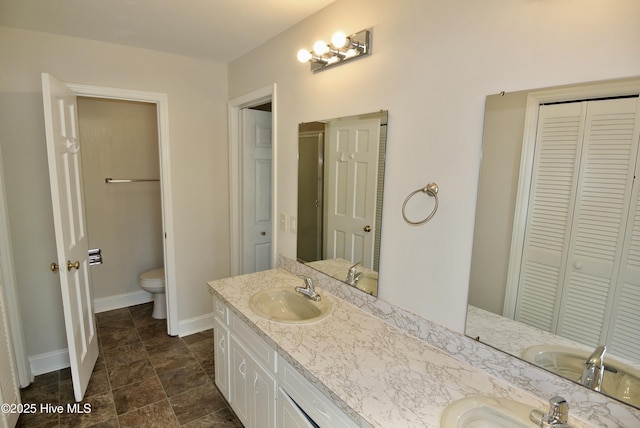 bathroom featuring double vanity, a closet, toilet, a sink, and baseboards