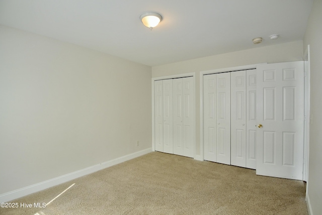 unfurnished bedroom featuring carpet, baseboards, and multiple closets