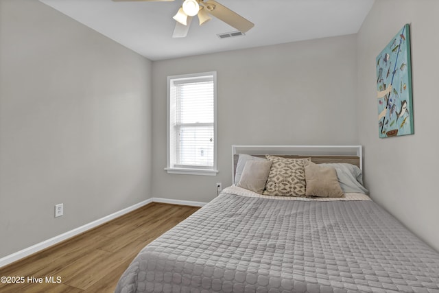 bedroom with a ceiling fan, wood finished floors, visible vents, and baseboards