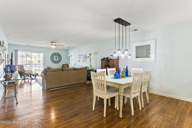 dining room with a ceiling fan, visible vents, baseboards, a fireplace, and dark wood-style flooring