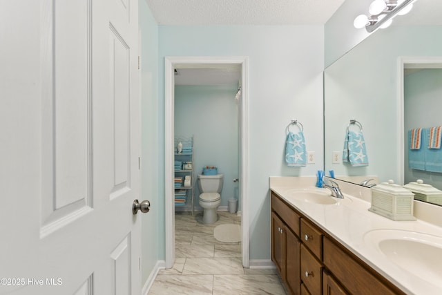 bathroom featuring a sink, a textured ceiling, marble finish floor, and double vanity