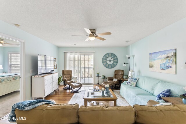 living room featuring visible vents, a textured ceiling, a ceiling fan, and wood finished floors