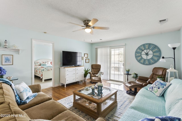 living room with a ceiling fan, wood finished floors, visible vents, and a textured ceiling