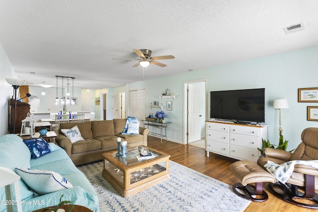 living room with ceiling fan, wood finished floors, visible vents, and a textured ceiling