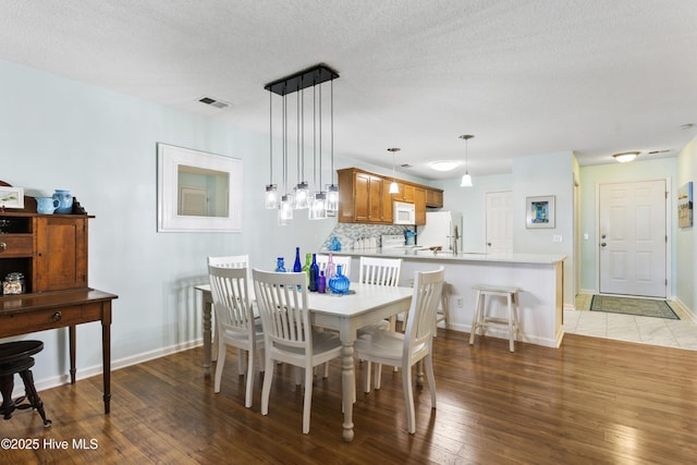 dining area with visible vents, a textured ceiling, baseboards, and hardwood / wood-style floors