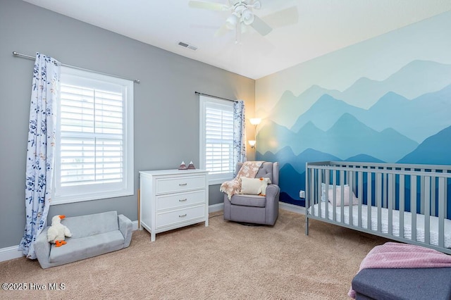 carpeted bedroom featuring a nursery area, ceiling fan, baseboards, and visible vents