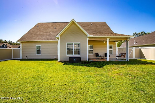 rear view of property featuring a fenced backyard, a shingled roof, a yard, and a patio area