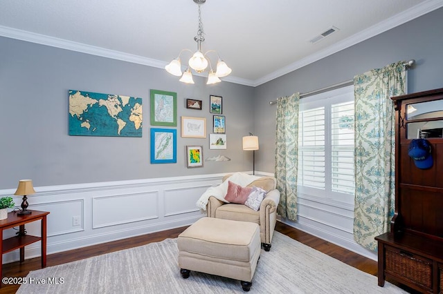living area with visible vents, wainscoting, wood finished floors, an inviting chandelier, and ornamental molding