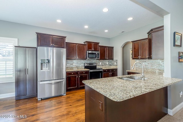 kitchen featuring a sink, arched walkways, stainless steel appliances, baseboards, and a peninsula