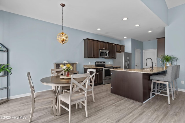 kitchen featuring appliances with stainless steel finishes, dark brown cabinetry, a sink, light stone countertops, and baseboards