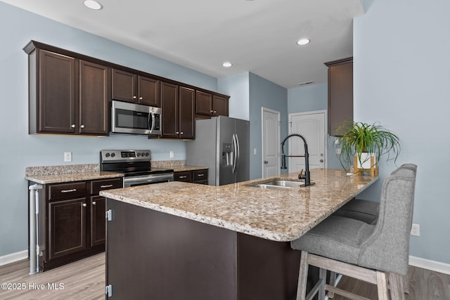 kitchen with stainless steel appliances, a sink, light stone counters, and dark brown cabinetry