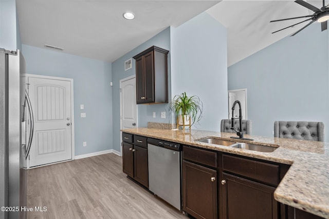 kitchen featuring a sink, dark brown cabinets, appliances with stainless steel finishes, light stone countertops, and light wood finished floors