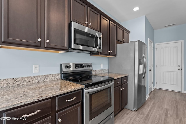 kitchen featuring light stone counters, light wood-style flooring, stainless steel appliances, visible vents, and dark brown cabinets