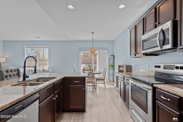 kitchen with dark brown cabinetry, appliances with stainless steel finishes, light stone counters, and a sink