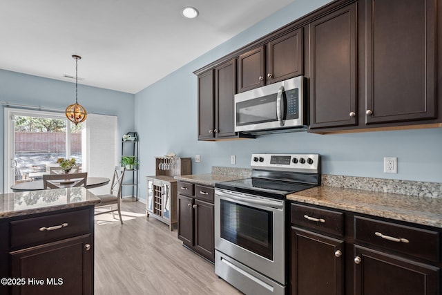 kitchen featuring dark brown cabinetry, light wood-style floors, appliances with stainless steel finishes, light stone countertops, and pendant lighting