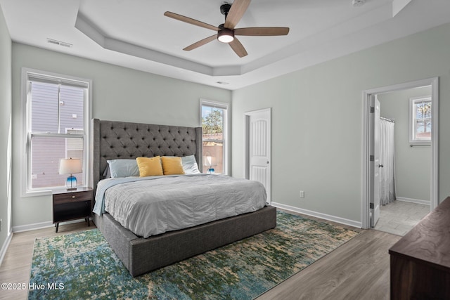 bedroom featuring a tray ceiling, wood finished floors, visible vents, and baseboards