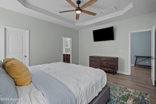 bedroom with a raised ceiling, visible vents, a ceiling fan, wood finished floors, and baseboards