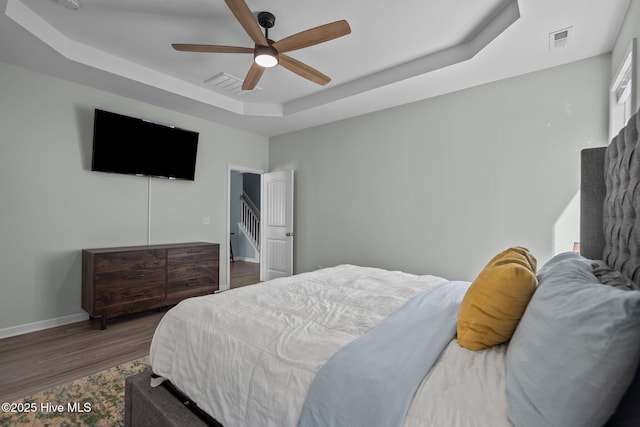 bedroom featuring baseboards, visible vents, a ceiling fan, a raised ceiling, and wood finished floors