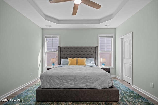 bedroom with wood finished floors, a raised ceiling, visible vents, and baseboards