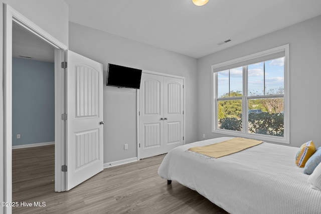 bedroom with a closet, visible vents, baseboards, and wood finished floors