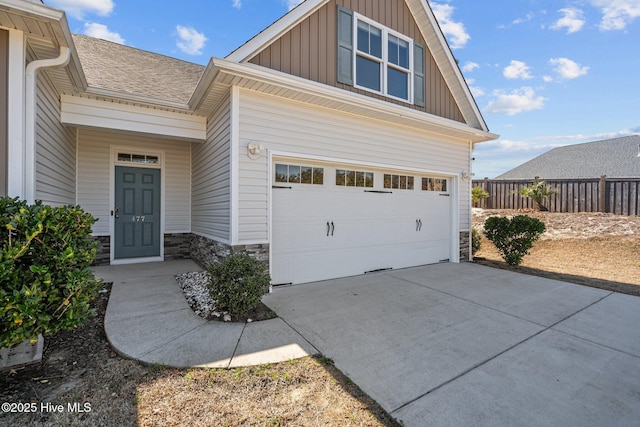 exterior space with a shingled roof, concrete driveway, board and batten siding, fence, and stone siding