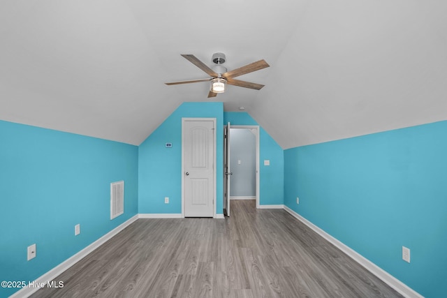 additional living space featuring lofted ceiling, wood finished floors, a ceiling fan, visible vents, and baseboards