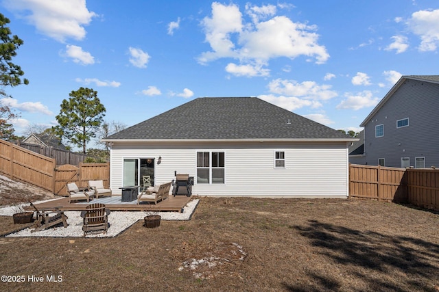 back of property with a fenced backyard, roof with shingles, a lawn, and a wooden deck