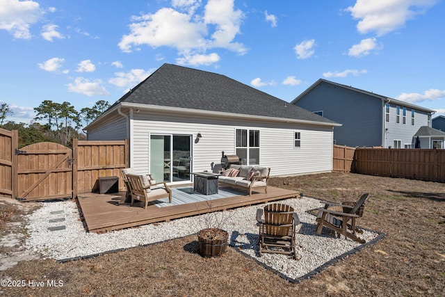 back of property with a shingled roof, fence, a wooden deck, a gate, and an outdoor living space with a fire pit