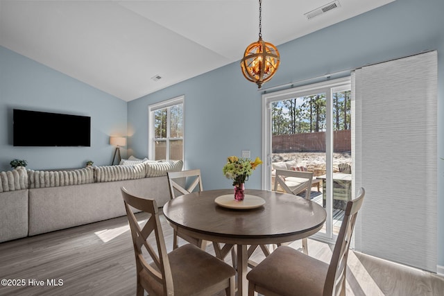 dining area featuring plenty of natural light, visible vents, vaulted ceiling, and wood finished floors