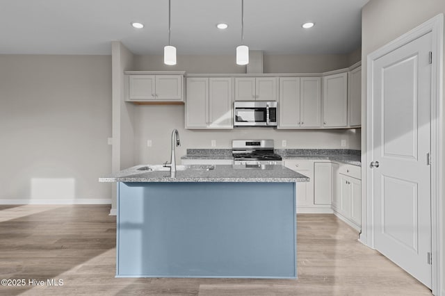 kitchen with pendant lighting, light wood finished floors, appliances with stainless steel finishes, a kitchen island with sink, and a sink