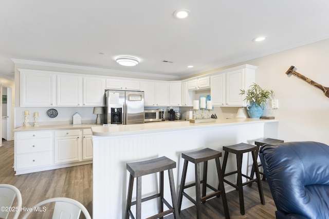 kitchen with stainless steel appliances, a breakfast bar, ornamental molding, and wood finished floors