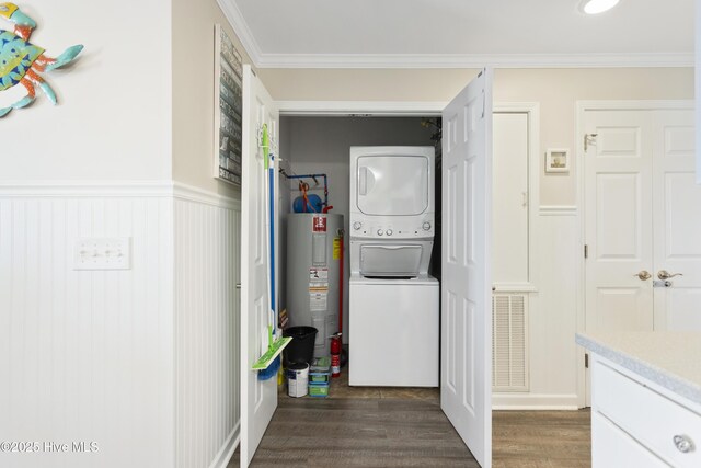 laundry room with a wainscoted wall, dark wood-type flooring, electric water heater, stacked washing maching and dryer, and laundry area