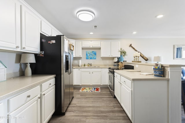 kitchen featuring stainless steel appliances, a peninsula, white cabinets, light countertops, and ornamental molding