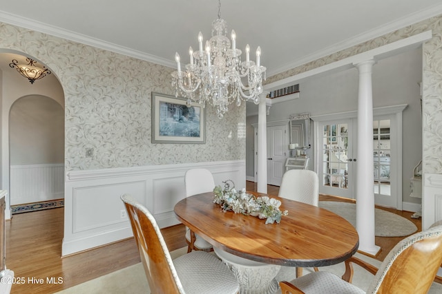 dining area with arched walkways, a wainscoted wall, ornamental molding, wood finished floors, and wallpapered walls