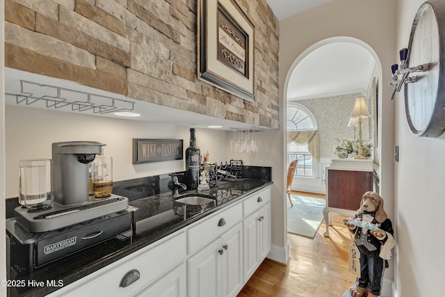 kitchen featuring arched walkways, white cabinets, a sink, wood finished floors, and dark stone counters