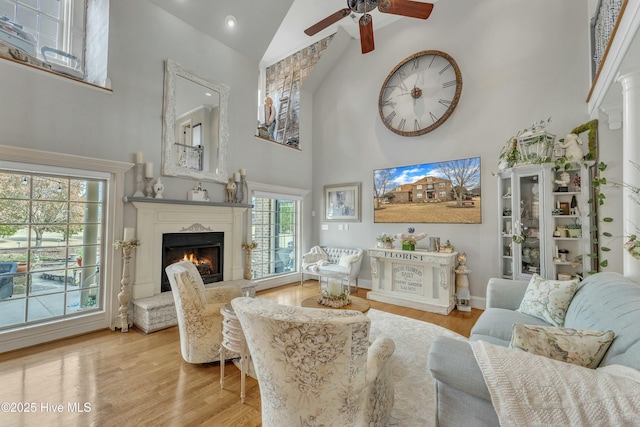 living area with a lit fireplace, high vaulted ceiling, wood finished floors, and a ceiling fan