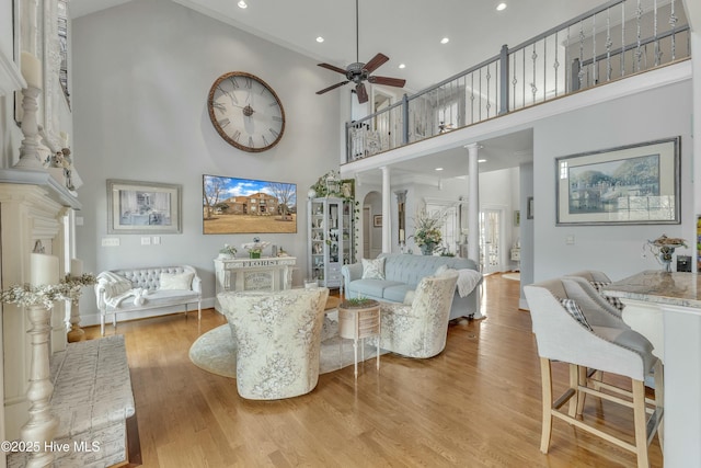 living area featuring arched walkways, a high ceiling, ceiling fan, wood finished floors, and ornate columns