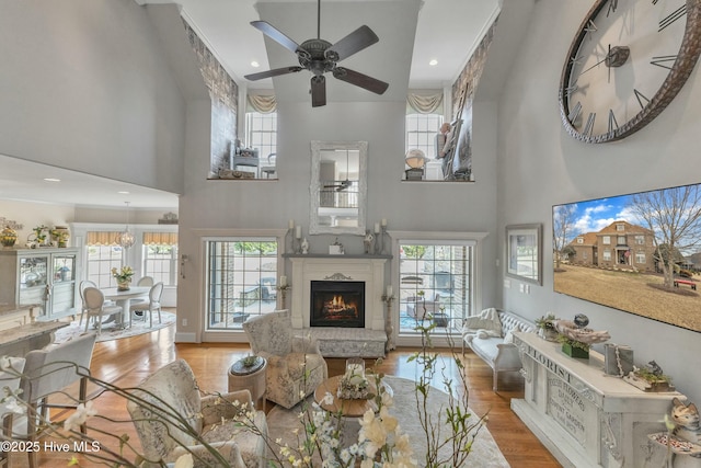 living room featuring ceiling fan, a warm lit fireplace, plenty of natural light, and wood finished floors