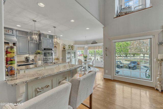 kitchen with light stone counters, gray cabinets, light wood-style flooring, and decorative light fixtures