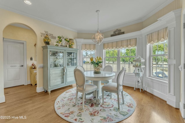 dining room with arched walkways, ornamental molding, an inviting chandelier, and light wood-style floors